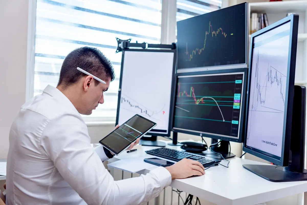 A man at a desk reading charts on four monitors and a tablet